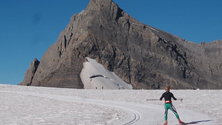 A man skis on the snow in front of a mountain tip. 