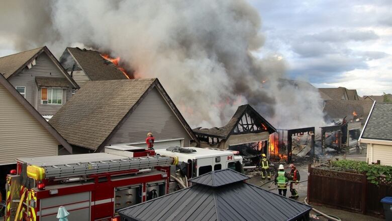 Smoke is seen coming from the smouldering wreckage of a home, with firefighters and a fire truck present.