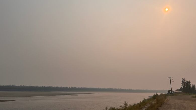 A smoky haze hangs over Old Crow, Yukon, on Wednesday. The riverbank, river and an orange sun are shown in this photo. Residents report that the smoke has been so thick at times that they can't see across the river.