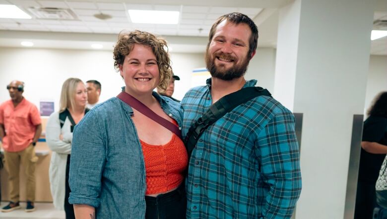 A smiling couple, arm in arm, at an airport.