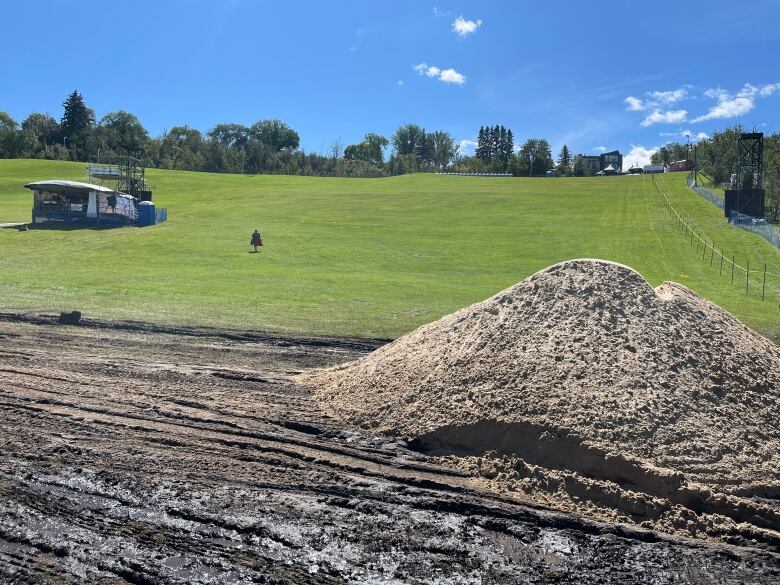 A pile of sand sits atop of a muddy path. A grassy hill is visible in the background