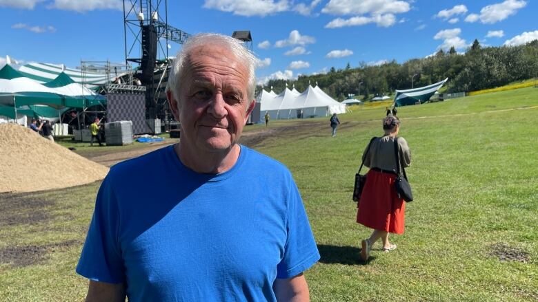 A man in a blue shirt stands before a grassy field.