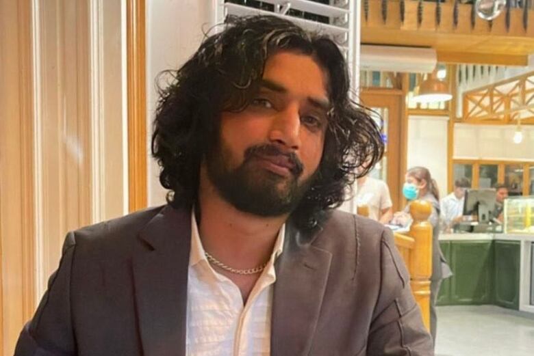 A man with dark wavy hair and a beard sits at a table.