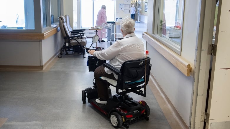 A woman in a long-term care home rides a mobility scooter.