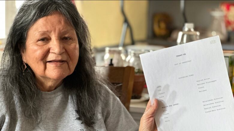 An older woman with greying hair holds up a paper.