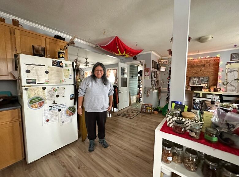 A woman wearing black plants and a grey sweater stands inside a house. A red flag hangs from the ceiling.