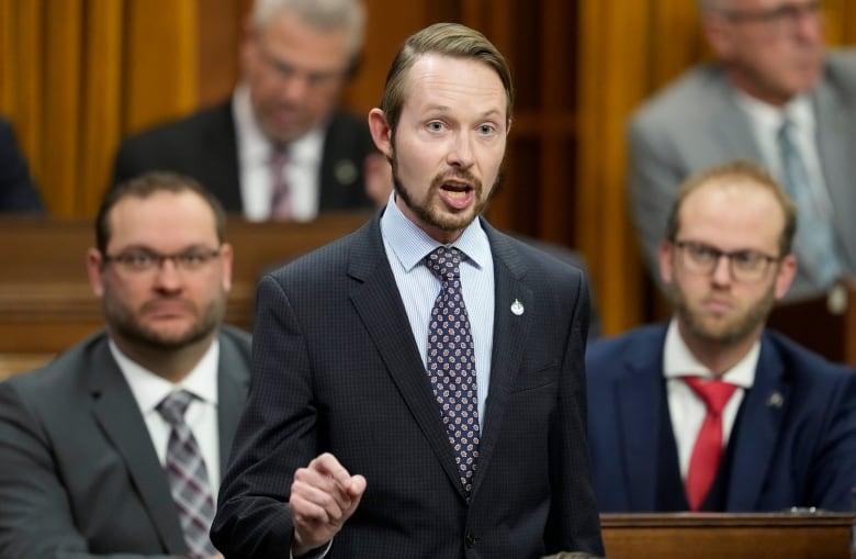 A man in a suit stands in the House of Commons chamber.