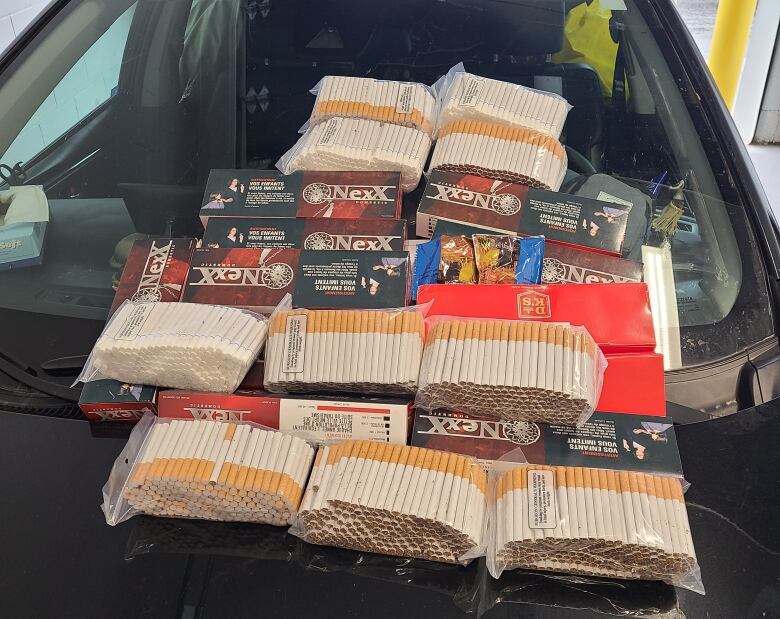 A photo shows clear plastic bags filled with cigarettes sitting on the hood of a car.