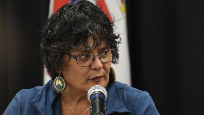 A close up of a woman in glasses speaking into a microphone.