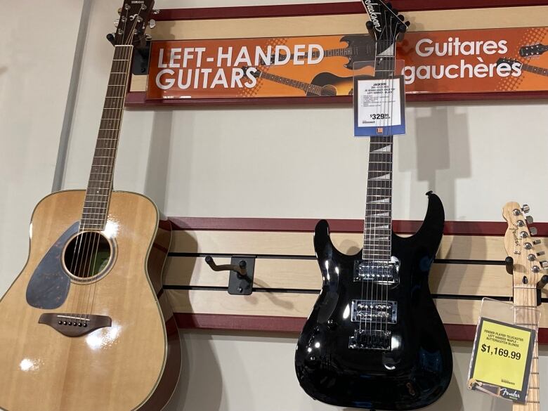 Two guitars hanging on a wall below a sign that reads 