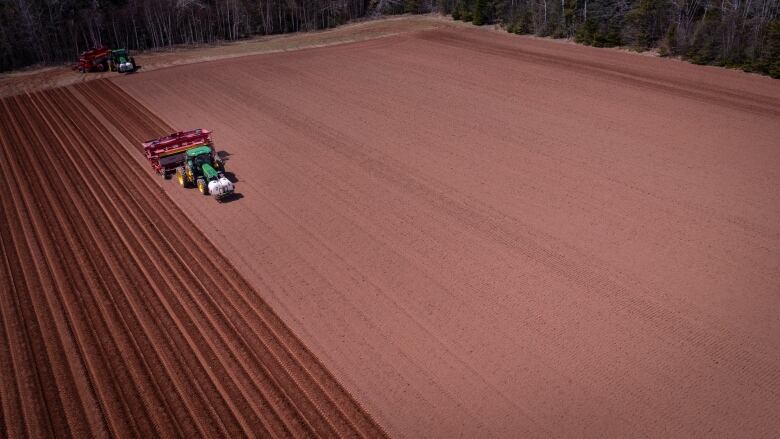 Aerial view of tractors planting potatoes and plowing a field in  Roseberry, P.E.I. on sunny afternoon