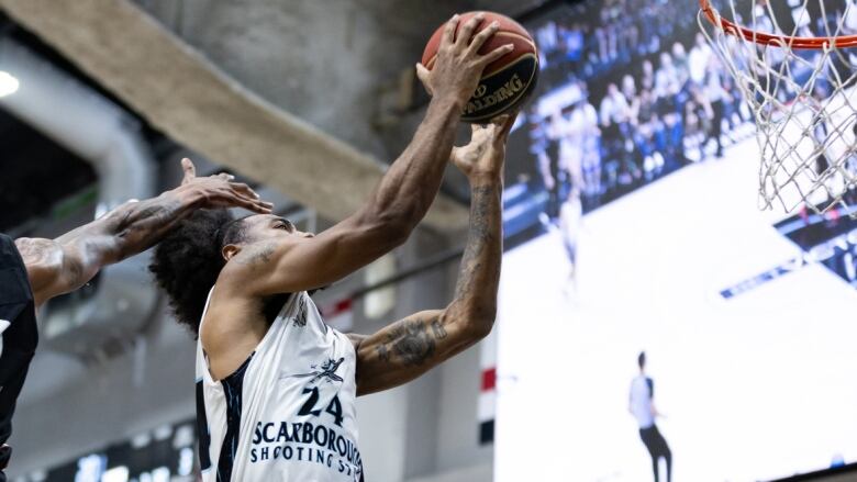 A male basketball player wearing number 24 leaps towards the basket while holding the ball with both hands as a defender attempts to block with his right hand.