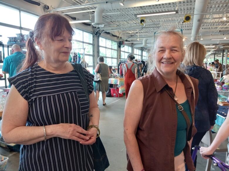 Two women standing with a busy market behind them.