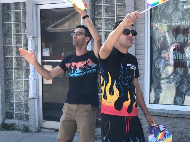 Two men wearing black t-shirts dancing and waving pride flags