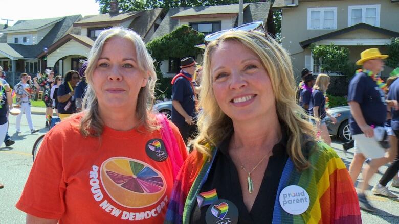 A woman wearing an orange t-shirt standing next to a woman draped in a pride flag