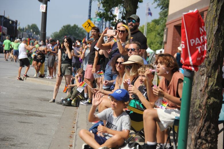 People standing and sitting on a street in support of a pride parade