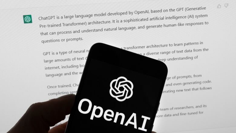  A hand holds up a smartphone with a black screen with the words OpenAI in white.