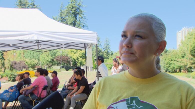 A woman stands at a fair in a yellow shirt. 