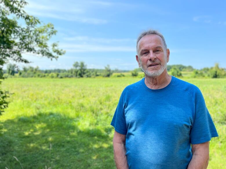 A man stands in a field and looks into the camera. 