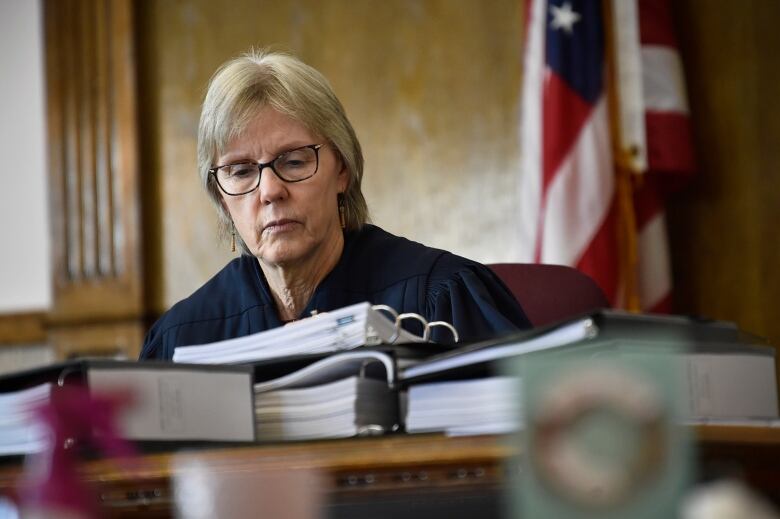 A woman with glasses in a judge's robes looks down at some binders.