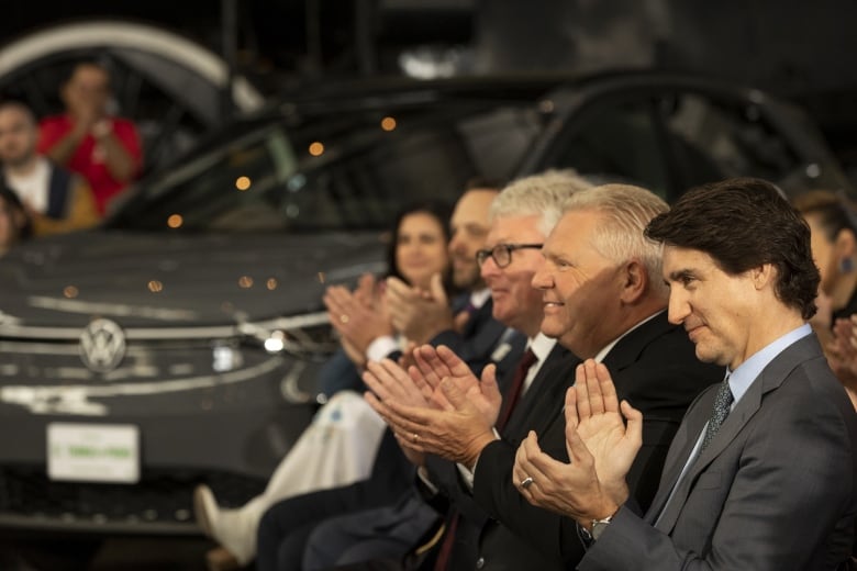 Men sit in a line clapping hands. 