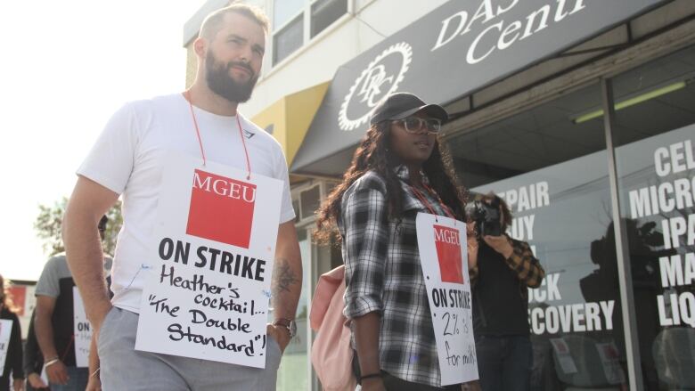 Two people walking with picket signs hanging on the front of their bodies.