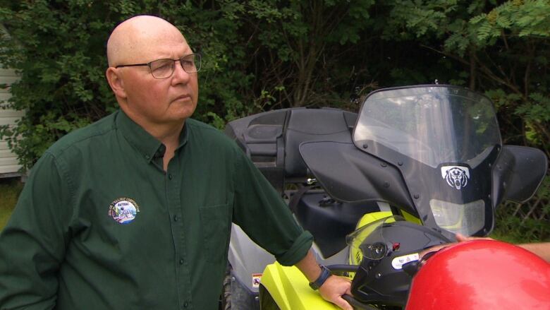 A man wearing a long sleeve green shirt stands next to a bright yellow ATV.