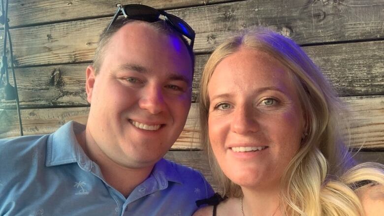 A couple smileS by a wooden wall in Maui.