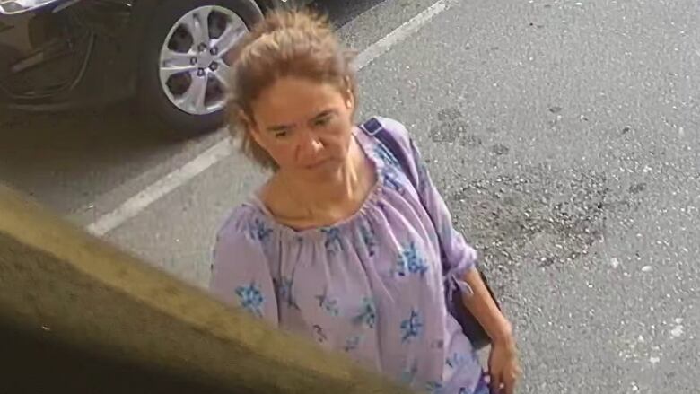 A woman wearing a purple top with blue flowers looks on in a surveillance camera still.