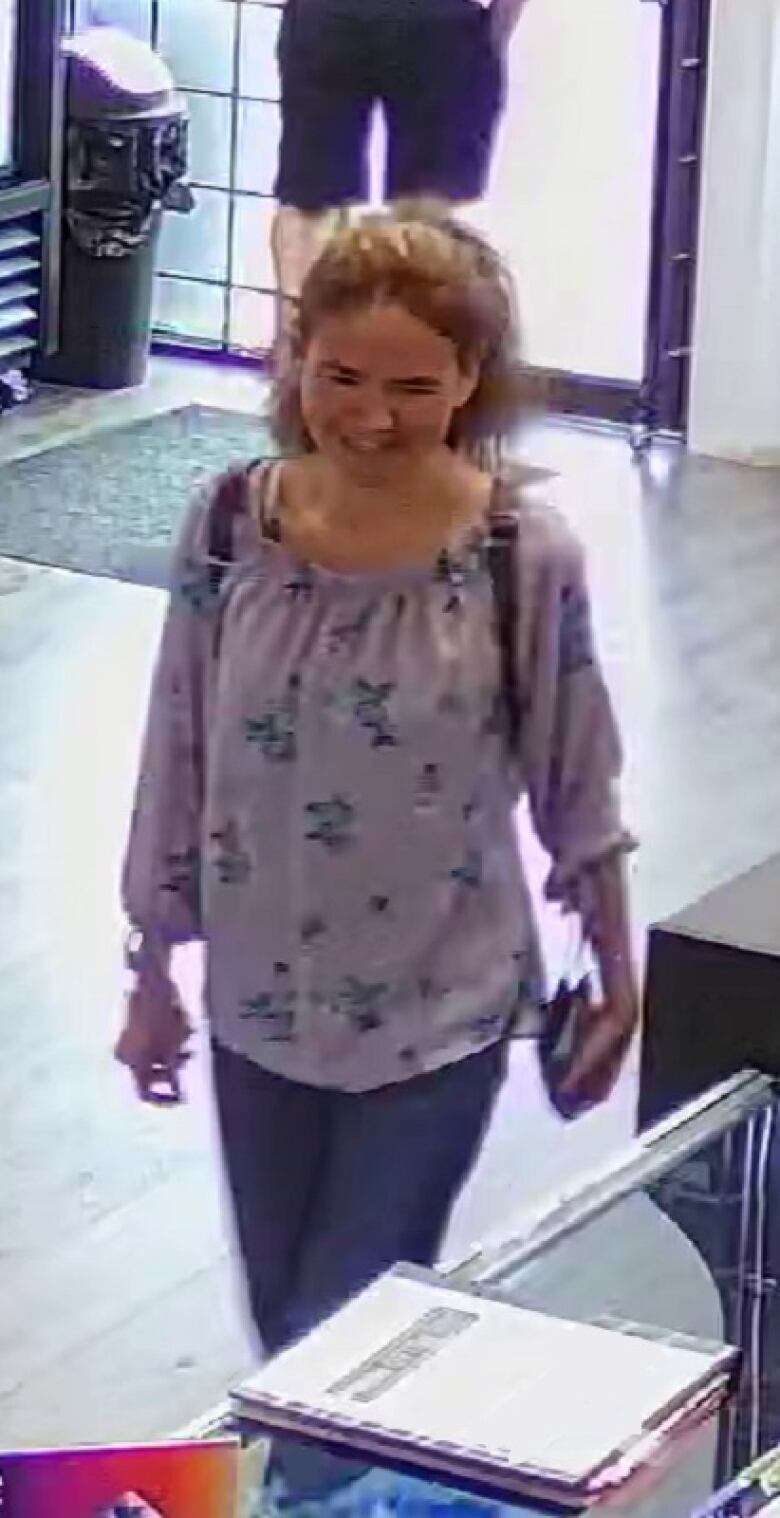 A woman wearing a purple top with blue flowers looks on in a surveillance camera still.