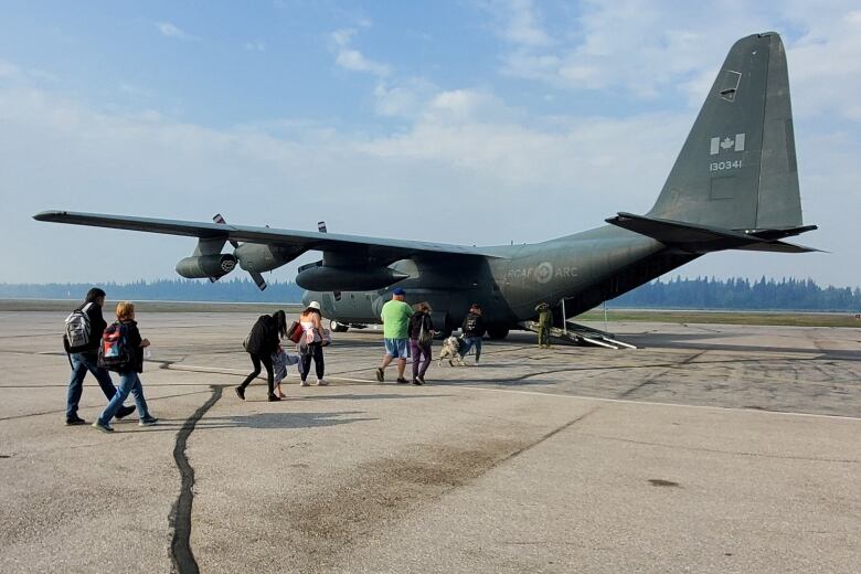 A group of people walking toward a Canadian Forces plane on a tarmac to be evacuated from Hay River, N.W.T.