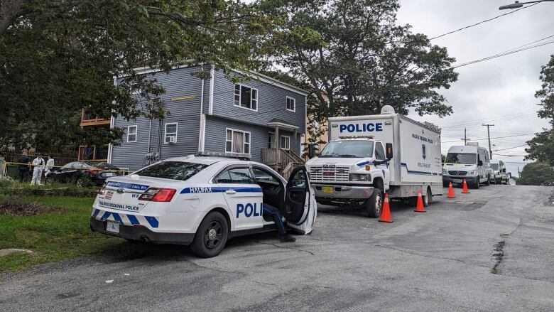 Cop vehicles can be seen parked in front of a blue house.