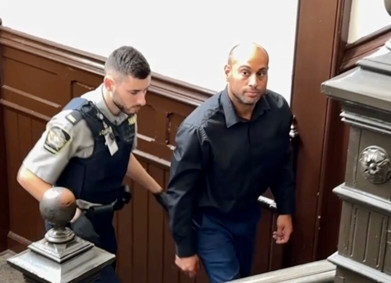 A police officer walks up the stairs behind a man wearing a jacket and jeans.