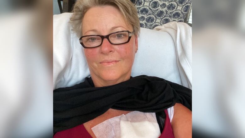 A woman lies down with a surgical pad on her chest.