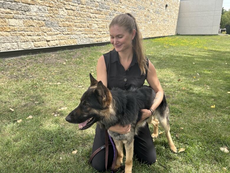 A woman in a black sleeveless shirt and black pants kneeled down beside a dog. 