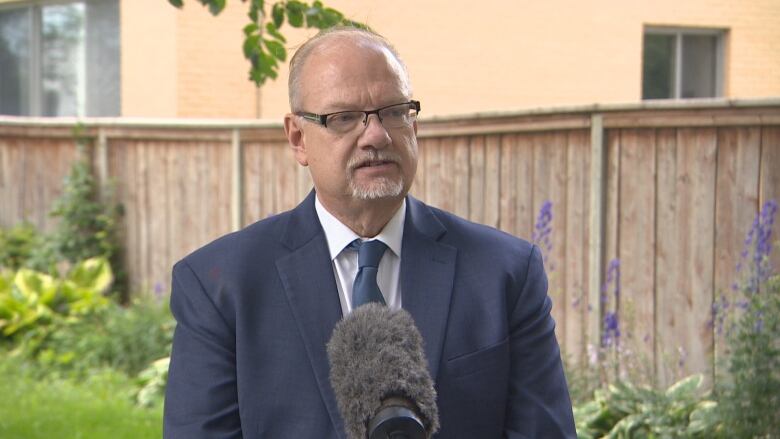 A man wearing glasses and a suit and tie speaks at a microphone.