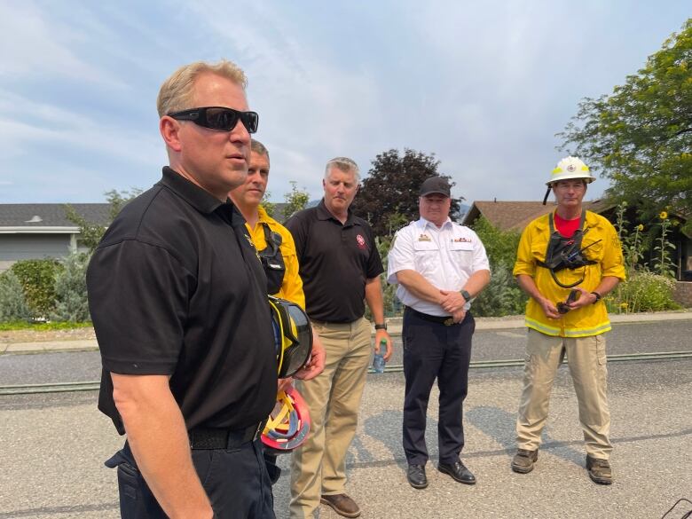 A line of white men, some of whom are wearing firefighting uniforms.