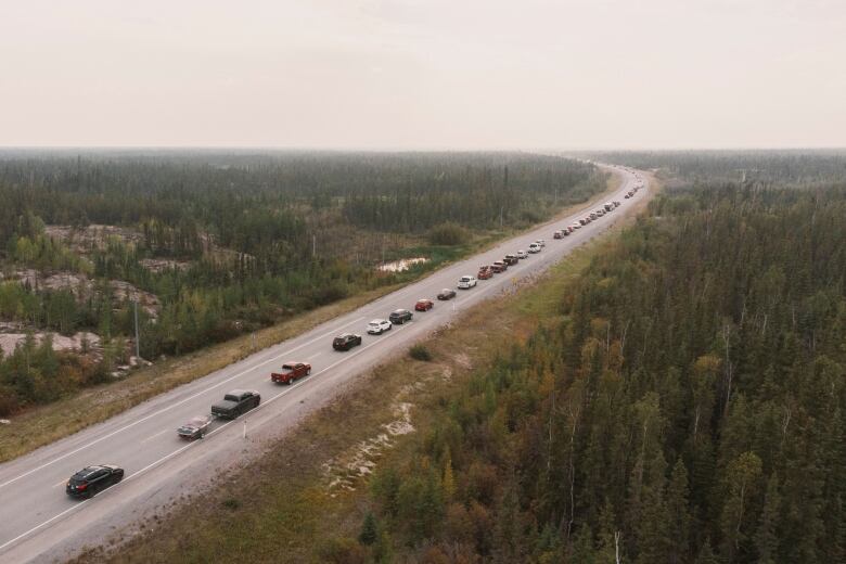 A long line of cars is seen driving in one direction on a rural highway.