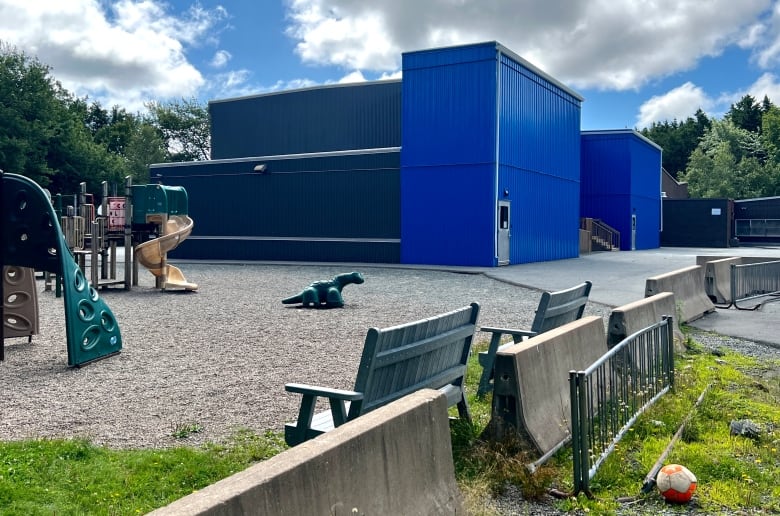 Part of a playground is shown on the left, with park benches in front, and large boxy blue buildings in the centre frame.