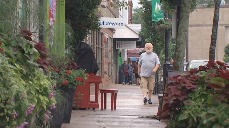 A man walks along a sidewalk lined with flowering plants.