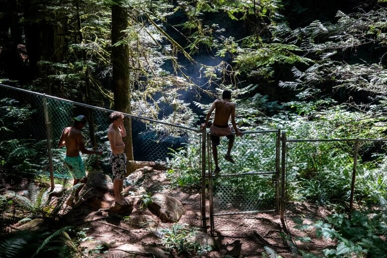 Cliff jumpers hop over a fence at Lynn Canyon Park.