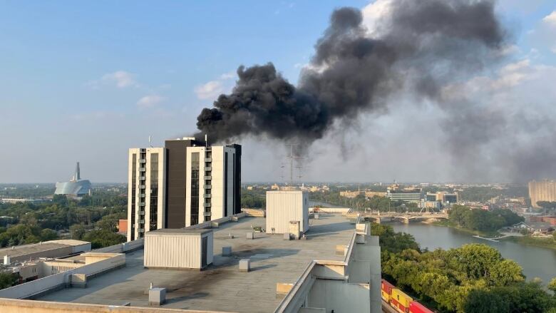 Black smoke comes from the top of an apartment building, with river and human rights museum in the background.