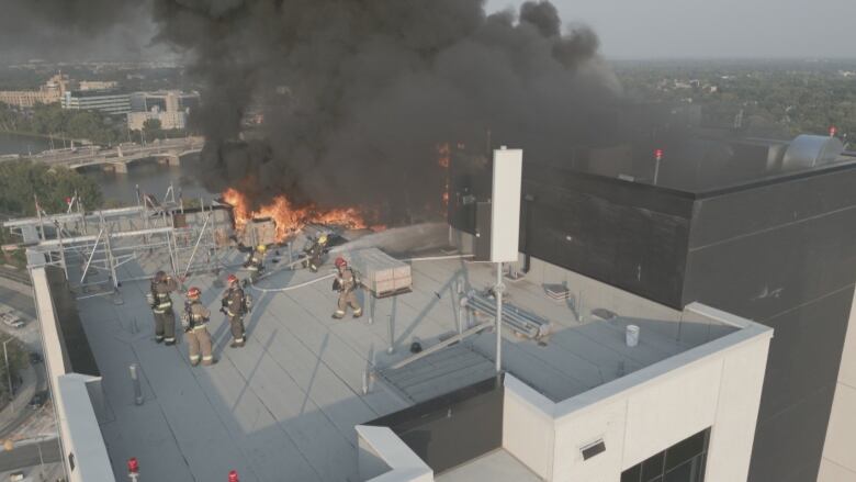 Six firefighters fight a fire on the roof of a high-rise building.