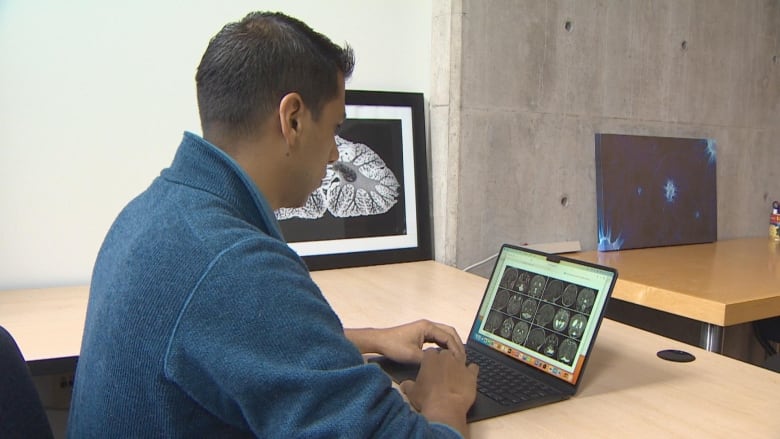 A researcher sits at his desk looking at brain scans on his computer.