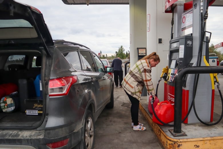 A woman fills up jerry-cans at a local gas station in Yellowknife, with the hatch to her vehicle open.