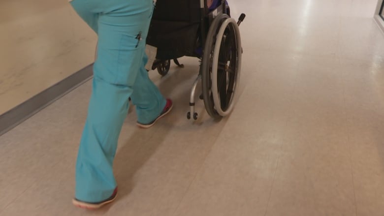 A health worker pushes a wheelchair down a hallway of a nursing home.