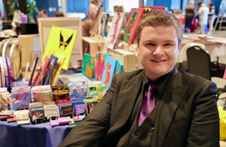 Connor stands in front of a table of with his art work displayed. 