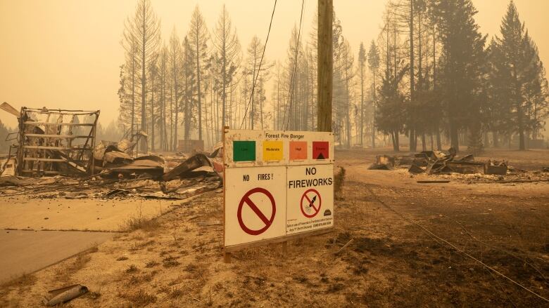 A sign showing an extreme wildfire warning stands amidst rubble.