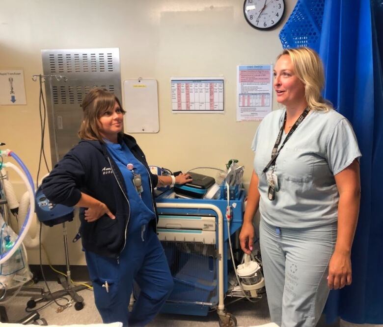 Two women wearing blue nursing scrubs standing in an empty hospital room