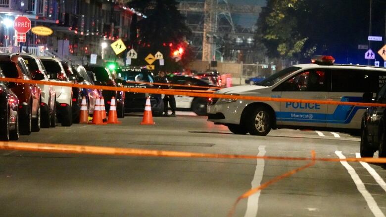 Police tape and police officers on site at a crime scene, surrounded by orange cones. 